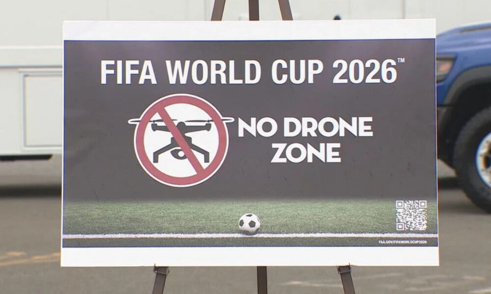 Sign for FIFA World Cup 2026 declaring 'No Drone Zone' with a crossed-out drone icon and a soccer ball on grass nearby on an easel poster, plus a QR code in the corner.