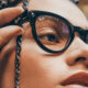 Close-up of a person wearing black Ray‑Ban glasses, adjusting a braided strap near the frame.