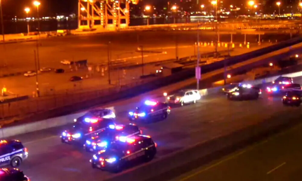 Nighttime scene with multiple police cars flashing red and blue lights on a city street near a highway.”