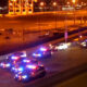 Nighttime scene with multiple police cars flashing red and blue lights on a city street near a highway.”