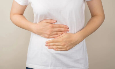 Person in a white shirt cups their abdomen with both hands, suggesting stomach pain or cramps.