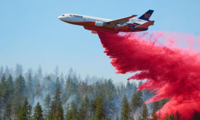 Air tanker plane releasing red fire retardant over a forest fire.