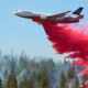 Air tanker plane releasing red fire retardant over a forest fire.