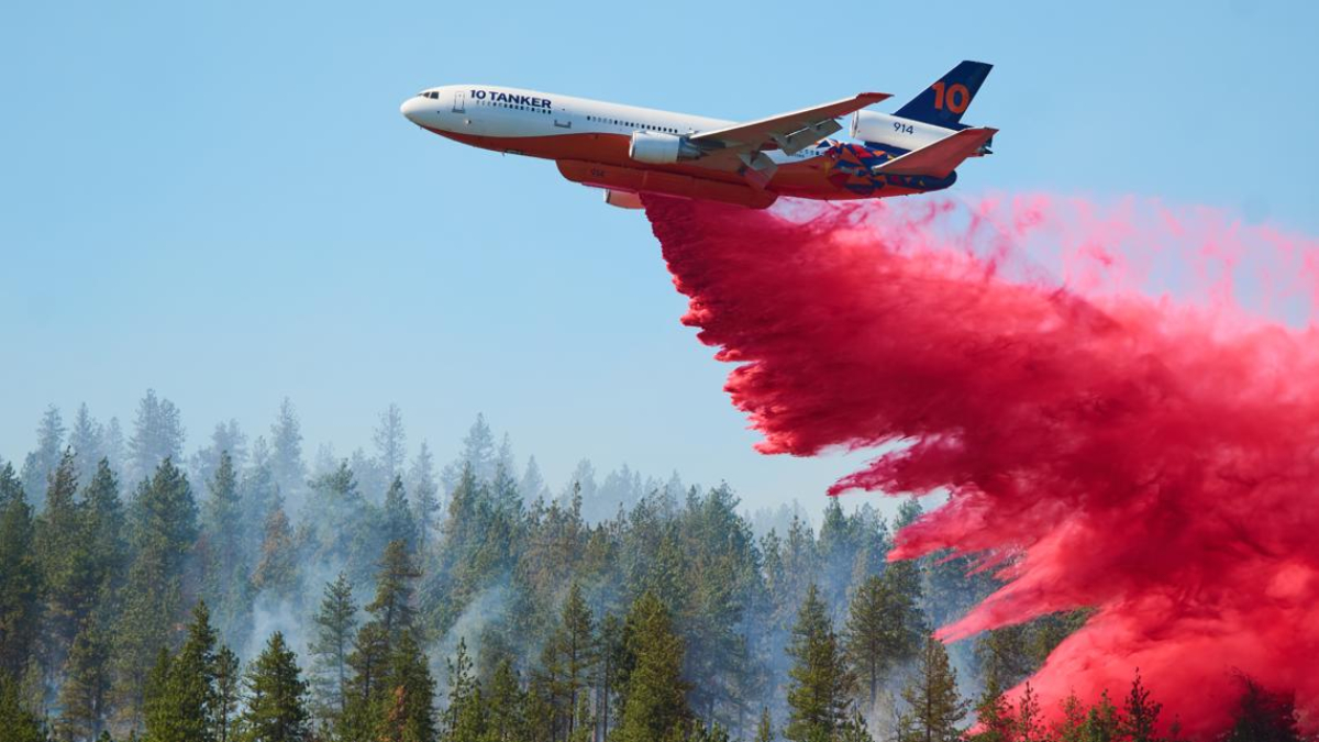 Air tanker plane releasing red fire retardant over a forest fire.