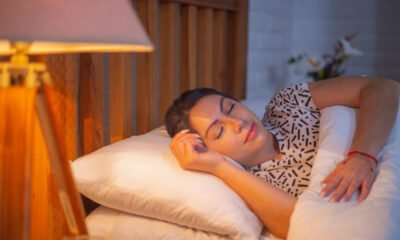Person sleeping on a white pillow in bed with a warm bedside lamp nearby.