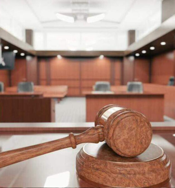 Wooden gavel resting on a sound block in a courtroom with wooden panels and benches in the background.
