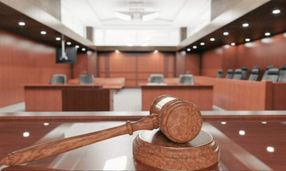 Wooden gavel resting on a sound block in a courtroom with wooden panels and benches in the background.