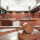 Wooden gavel resting on a sound block in a courtroom with wooden panels and benches in the background.
