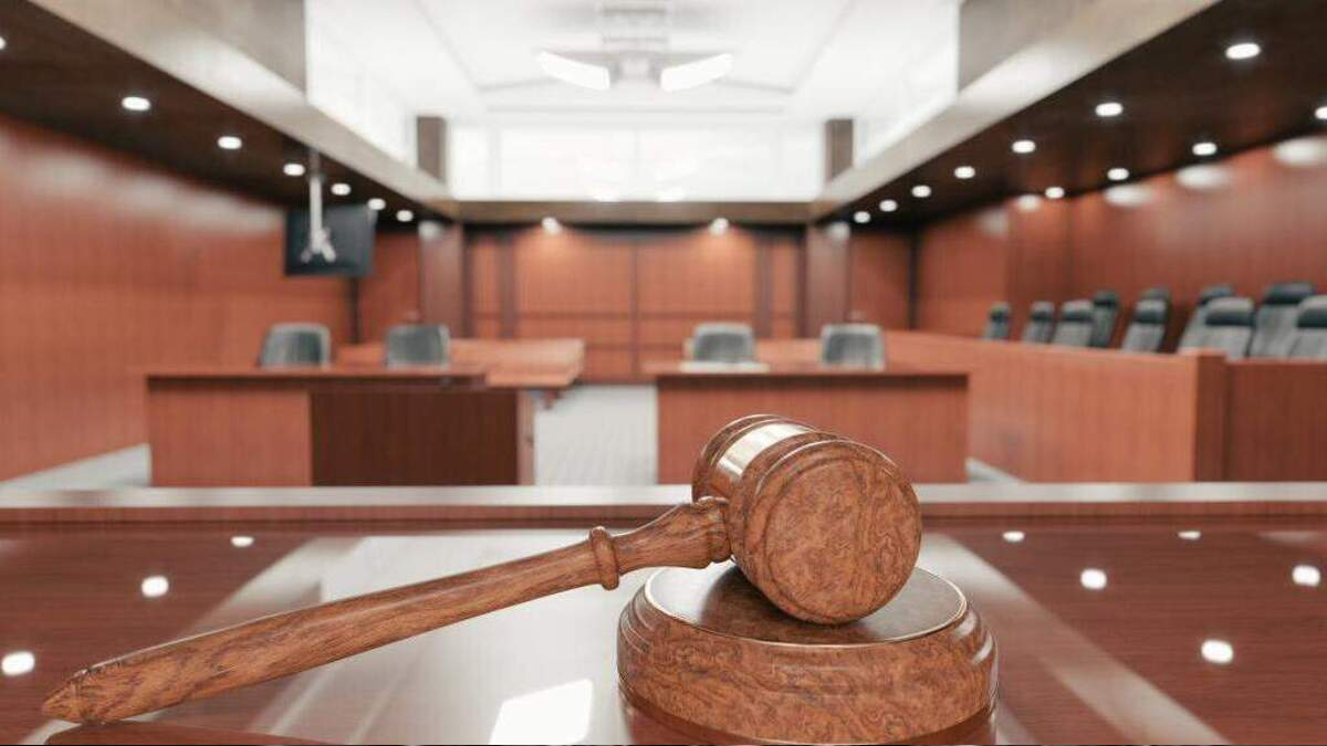 Wooden gavel resting on a sound block in a courtroom with wooden panels and benches in the background.