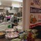 Volunteers in a kitchen preparing meals, with large bowls of chopped ingredients on the counter and a banner reading 'His Meal at Annie's Community Kitchen' in the background.