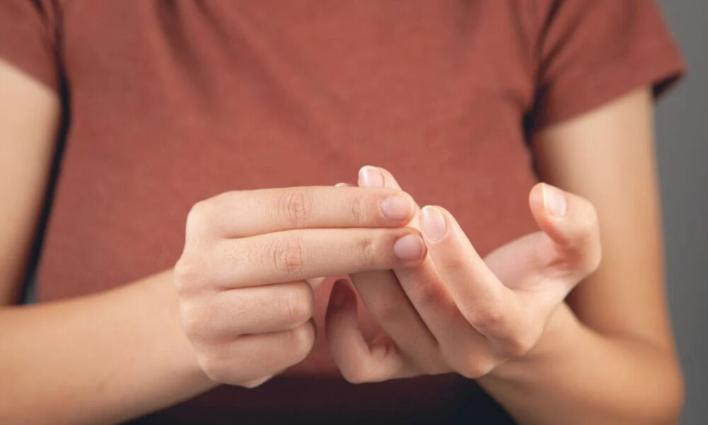 Close-up of hands handling a contact lens between the fingers in front of a maroon shirt.