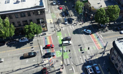 Aerial view of a city intersection with rainbow bike lanes and crosswalks, with cars and pedestrians nearby.