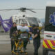 Emergency medical team transfers a patient on a stretcher toward an ambulance on a rooftop helipad beside a white-and-yellow helicopter (UW Medicine logo visible).