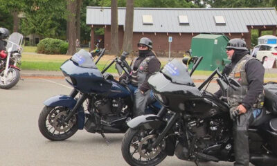 Two riders in black gear and helmets on dark touring motorcycles in a parking lot.