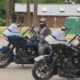 Two riders in black gear and helmets on dark touring motorcycles in a parking lot.