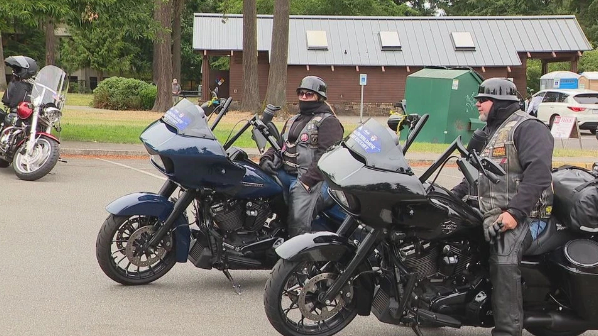 Two riders in black gear and helmets on dark touring motorcycles in a parking lot.