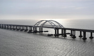 Long steel bridge with two curved arches spanning calm sea toward the horizon.