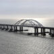 Long steel bridge with two curved arches spanning calm sea toward the horizon.