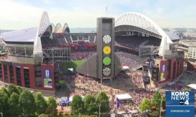 A large baseball stadium filled with fans, viewed from above, with a tall central tower displaying three colored disks and surrounding bleachers and field.