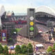 A large baseball stadium filled with fans, viewed from above, with a tall central tower displaying three colored disks and surrounding bleachers and field.