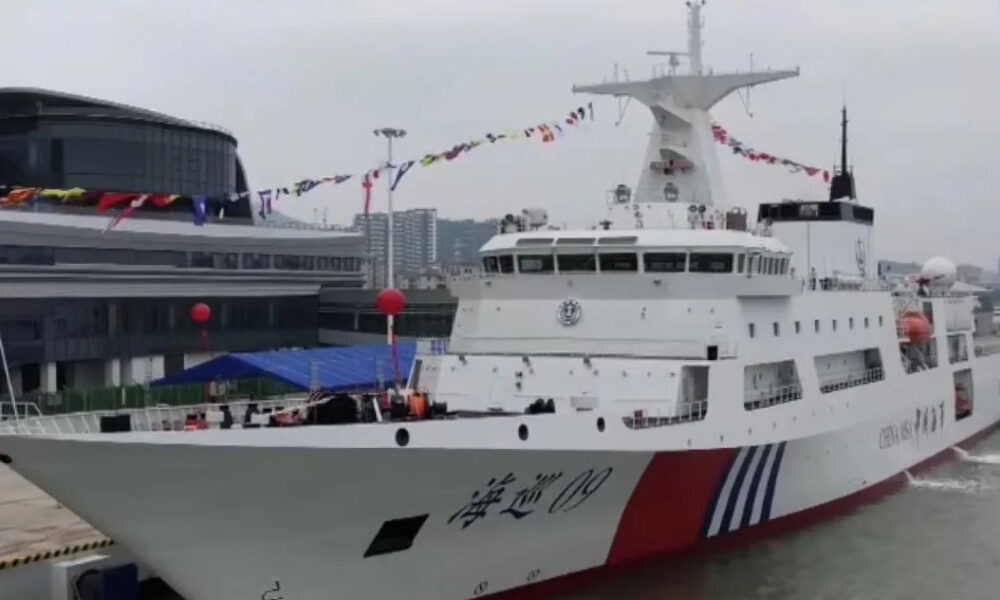 White passenger ferry docked at a harbor with colorful pennant flags strung along its mast and a red/blue hull accent.