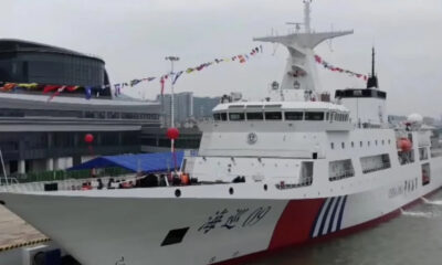White passenger ferry docked at a harbor with colorful pennant flags strung along its mast and a red/blue hull accent.