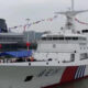 White passenger ferry docked at a harbor with colorful pennant flags strung along its mast and a red/blue hull accent.