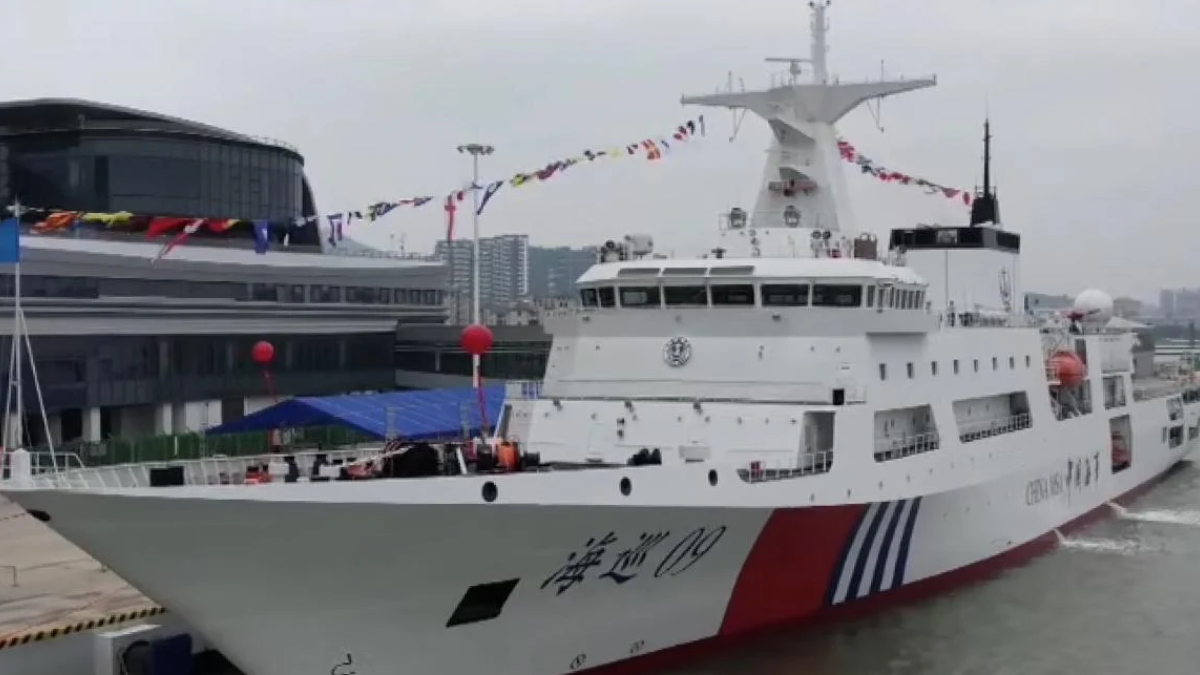 White passenger ferry docked at a harbor with colorful pennant flags strung along its mast and a red/blue hull accent.