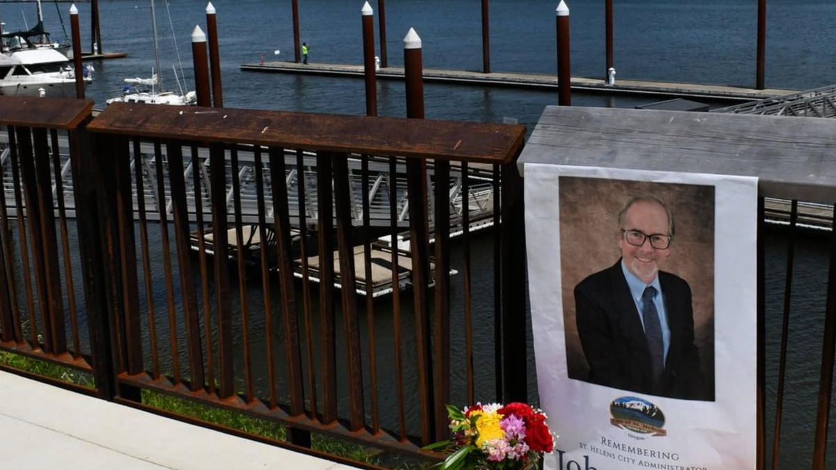 Poster of a man in a suit attached to a railing at a waterfront, with a bouquet of flowers nearby and boats in the background.