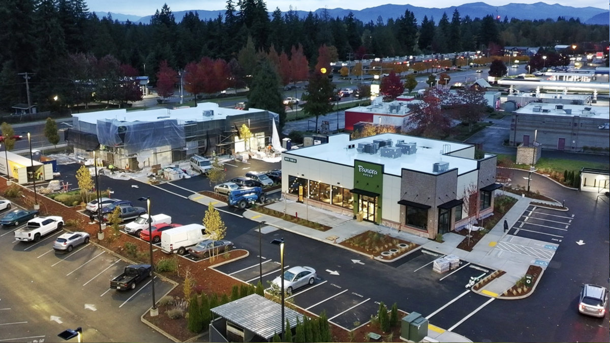 A Panera Bread storefront in a modern shopping center, with a parking lot and a construction site to the left, trees in autumn colors.