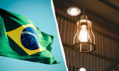 Brazil flag waving on the left with a blue sky, split by a curved divider from a warm pendant light on the right on a dark background.