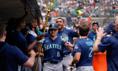 Seattle Mariners players celebrate in the dugout, high-fiving as a teammate with a golden trident leads the moment.