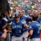 Seattle Mariners players celebrate in the dugout, high-fiving as a teammate with a golden trident leads the moment.