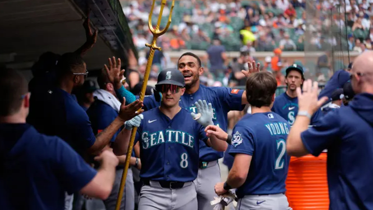 Seattle Mariners players celebrate in the dugout, high-fiving as a teammate with a golden trident leads the moment.