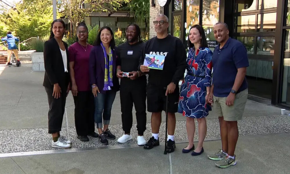 Group of eight diverse adults posing outdoors in front of a building, smiling for the photo.