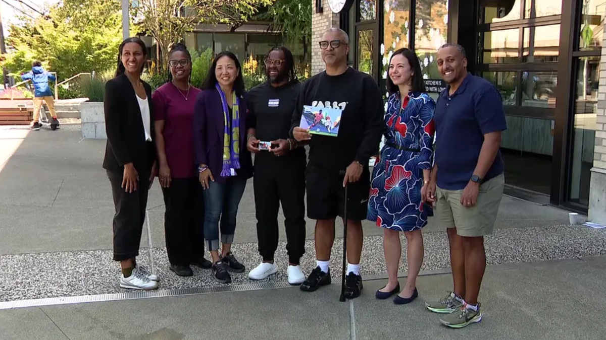 Group of eight diverse adults posing outdoors in front of a building, smiling for the photo.