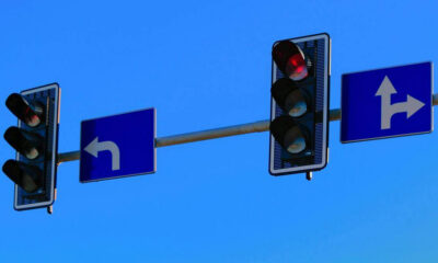 Traffic light signals at an intersection with a left-turn sign and a right/straight lane sign against a blue sky.