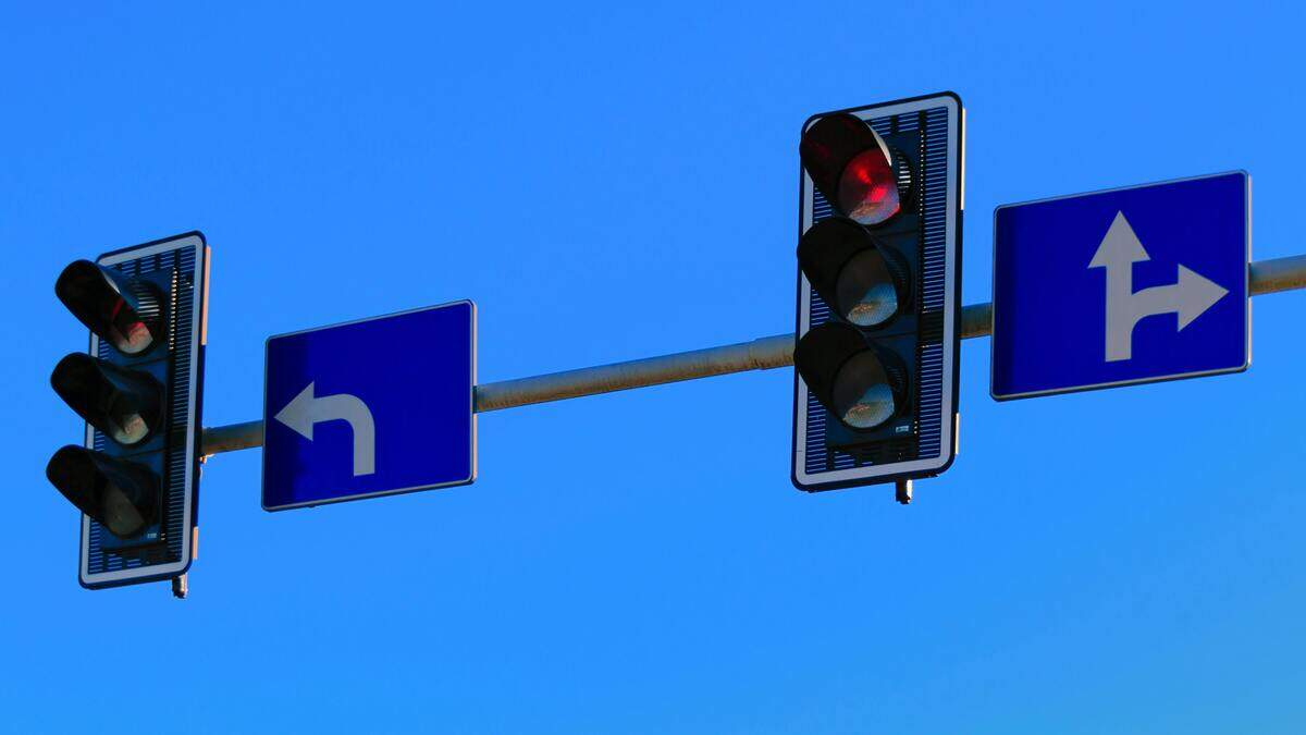 Traffic light signals at an intersection with a left-turn sign and a right/straight lane sign against a blue sky.