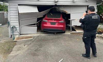 Police officer takes photos of a red SUV wedged inside a collapsed garage door after a crash.