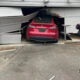 Police officer takes photos of a red SUV wedged inside a collapsed garage door after a crash.