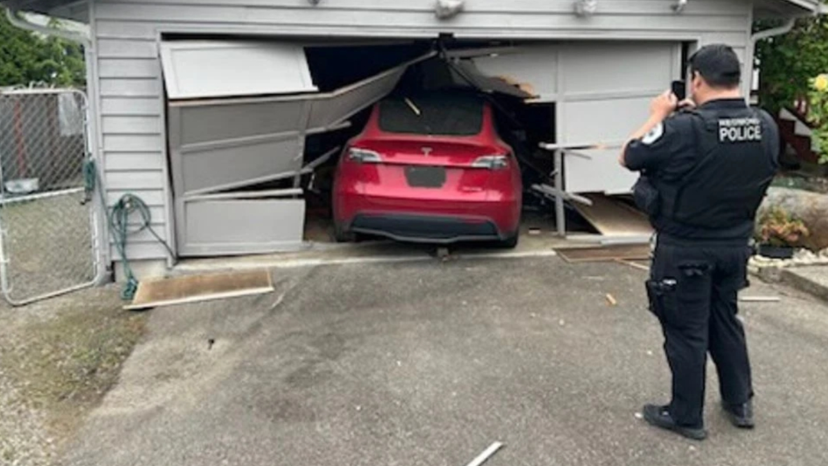 Police officer takes photos of a red SUV wedged inside a collapsed garage door after a crash.