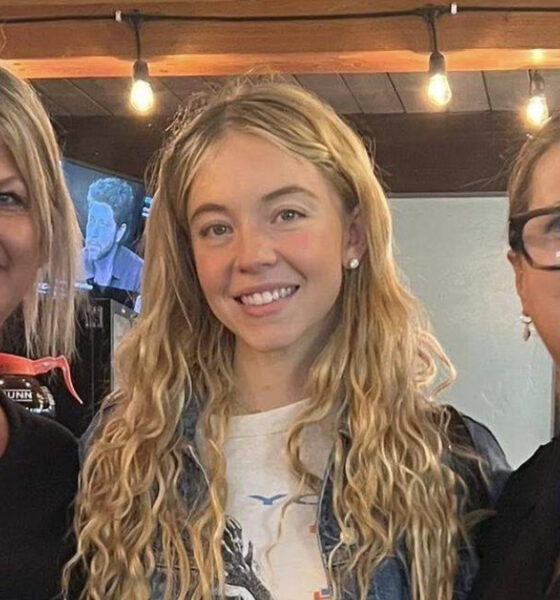 Three smiling women posing together indoors under warm string lights.