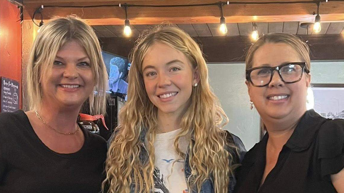 Three smiling women posing together indoors under warm string lights.