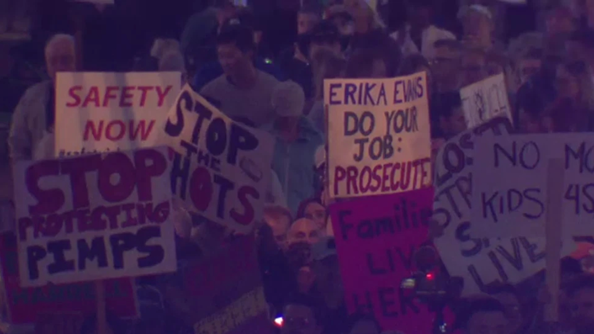 Crowd of protesters at a rally holding handwritten signs, including 'SAFETY NOW' and 'STOP THE SHOTS'.