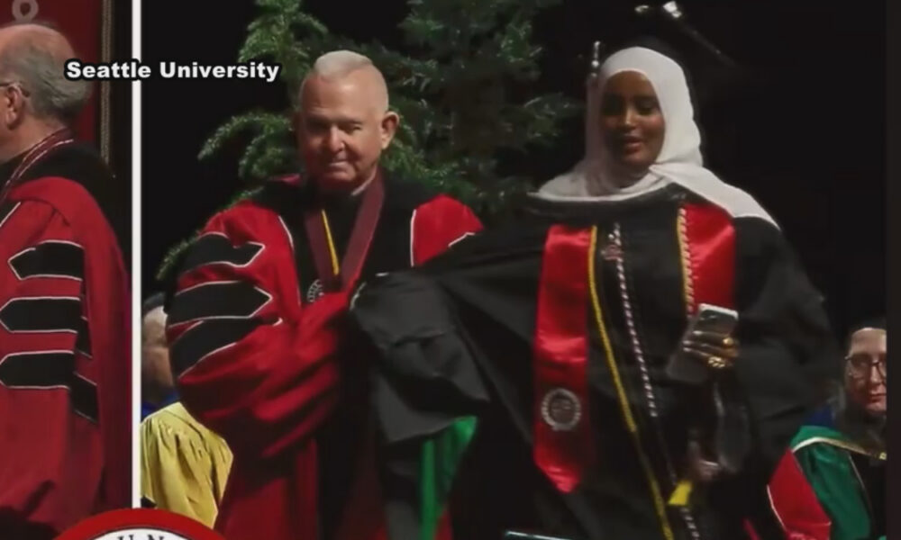 Graduate wearing a hijab in a black gown with red stole on stage during a Seattle University graduation ceremony.