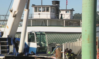 Harbor scene with a blue-and-white crane and a large white boat, workers in gear resting near a fence on the dock.