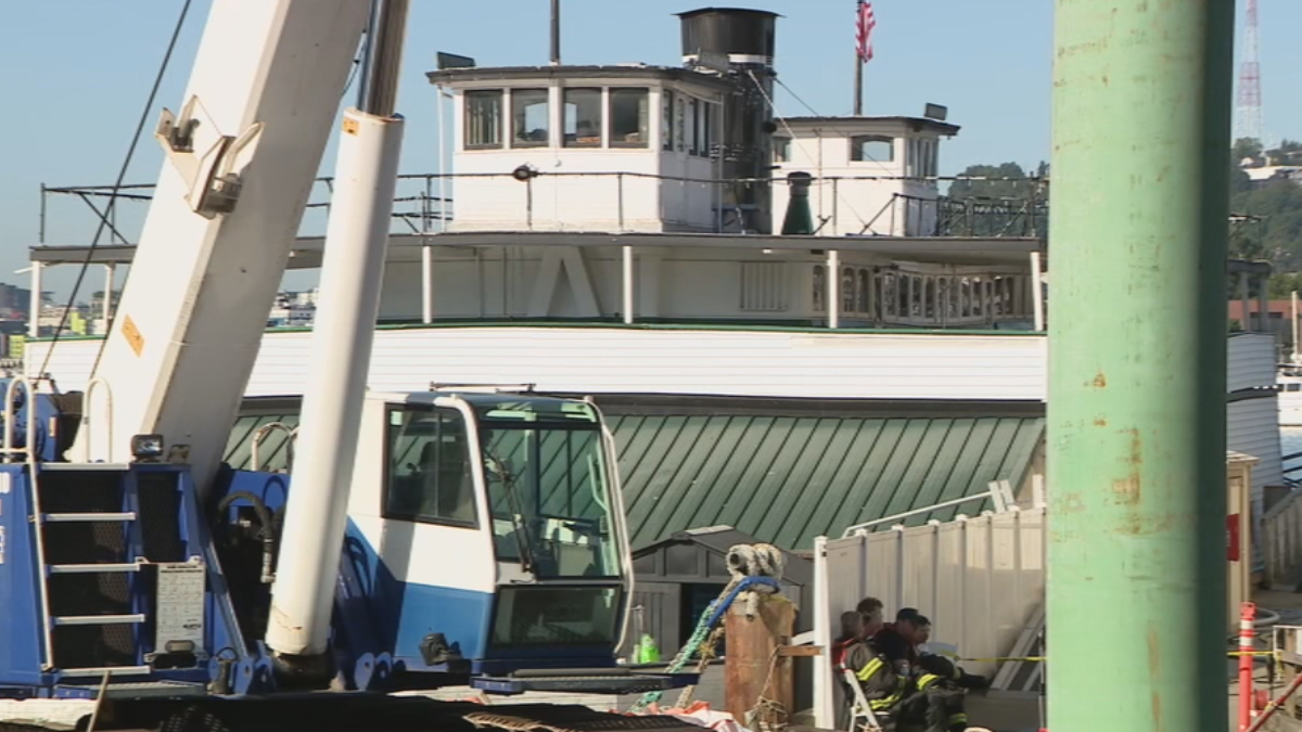 Harbor scene with a blue-and-white crane and a large white boat, workers in gear resting near a fence on the dock.