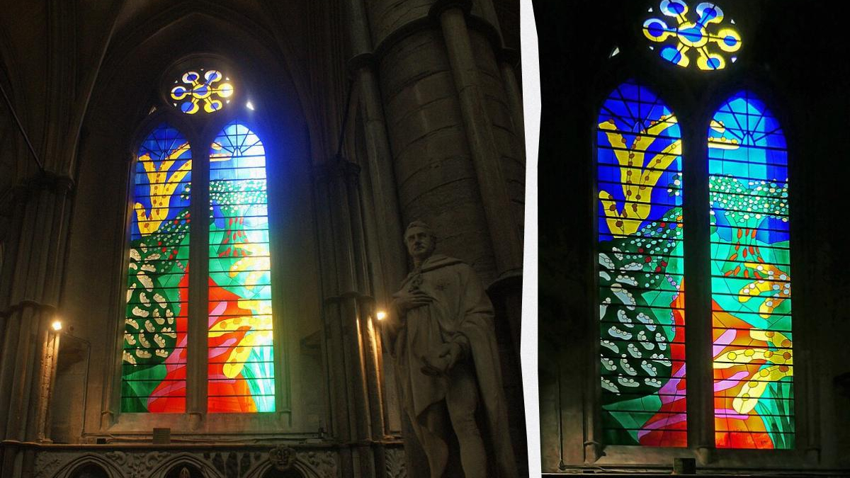 Stained glass church window with vibrant abstract landscape in blue, green, red, and yellow hues; stone arches nearby and a statue in foreground (left).