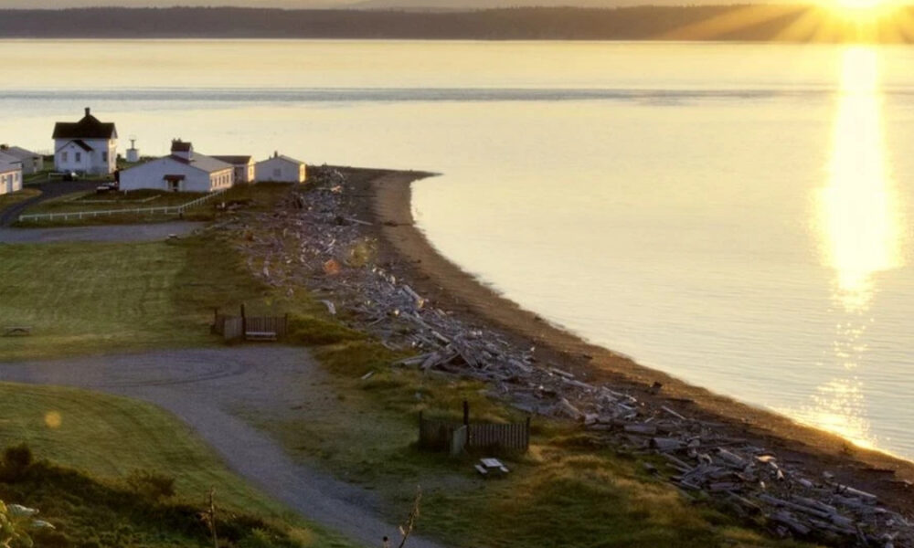 Sunset over a calm bay with a small coastal village on the left and a rocky beach along the water's edge.