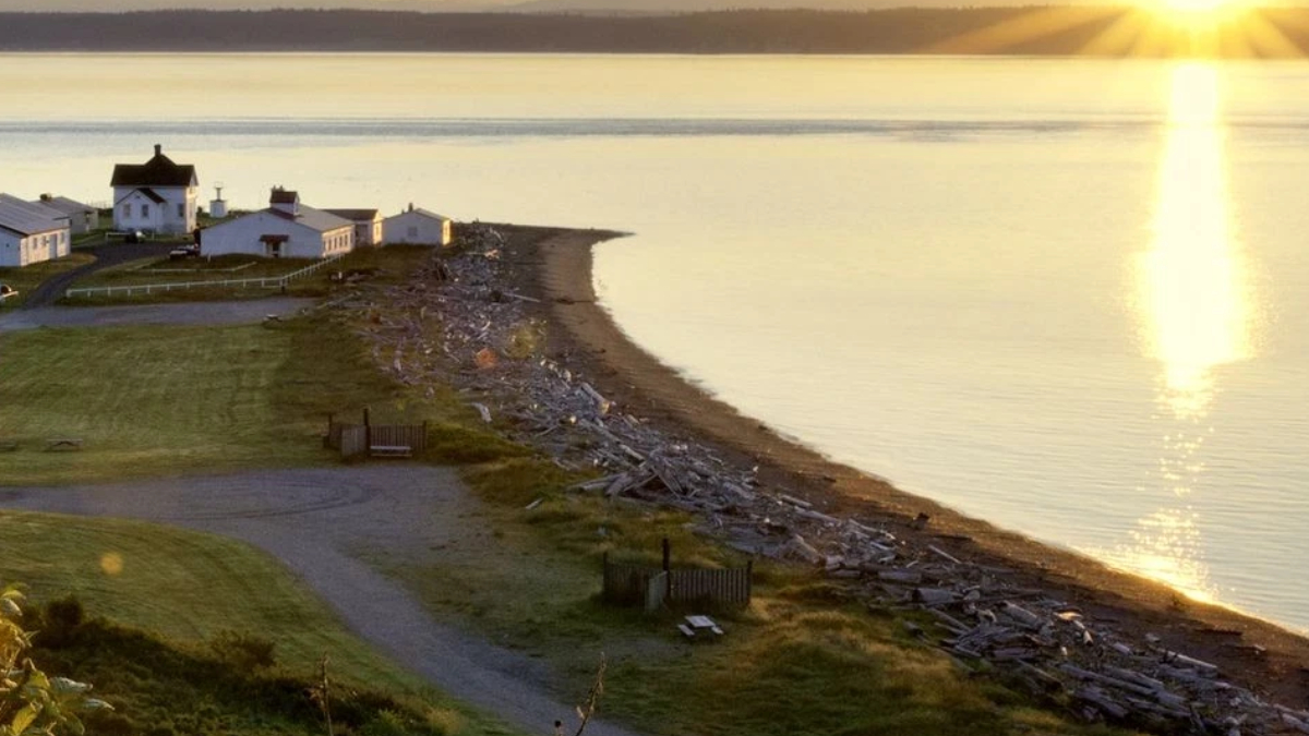 Sunset over a calm bay with a small coastal village on the left and a rocky beach along the water's edge.
